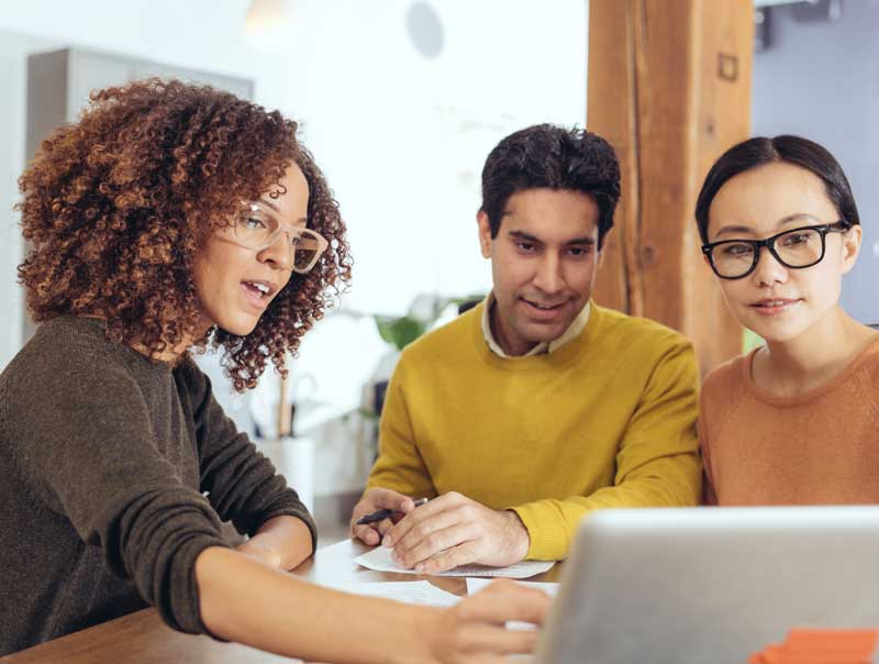 Three people around a laptop on a table