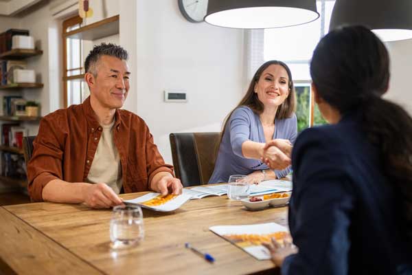 Three people sitting at a table looking at a pamphlet and having snack